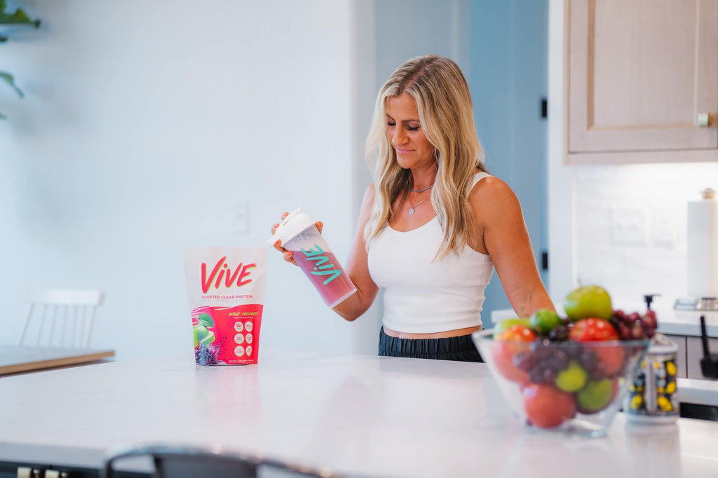Woman in a kitchen holding a container labeled 'Vive' with fruits on the counter.