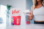Woman holding a 'Vive' protein powder container and a shaker with a pink background. Protein Shakes