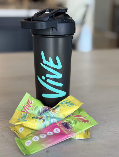 Black 'Vive' shaker bottle with colorful protein powder stick packs on a wooden surface. Protein Shakes